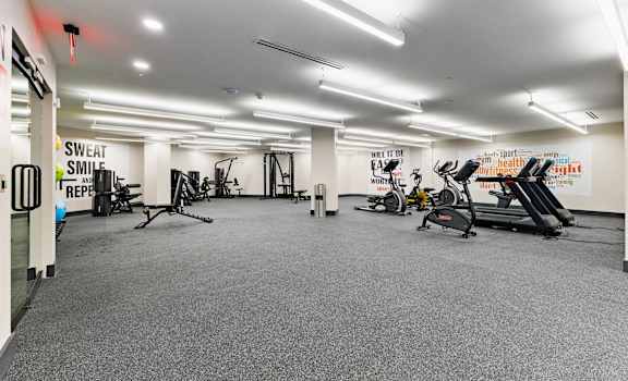 A gym with a variety of equipment including treadmills, stationary bikes, and weights.
