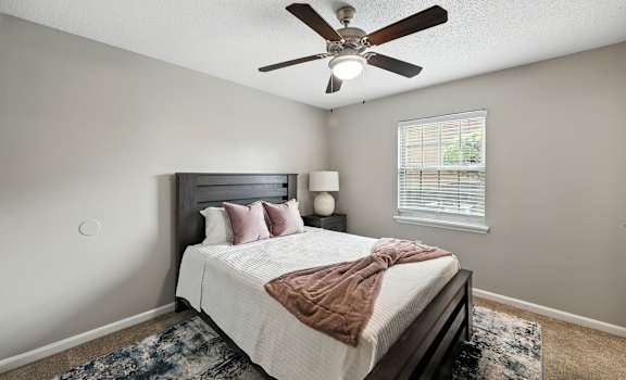 A bedroom with a bed, pillows, a blanket, a ceiling fan, and a rug.