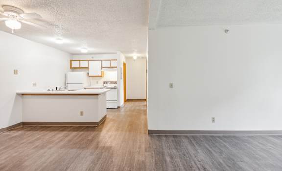 the living room and kitchen of an apartment with white walls and wood flooring
