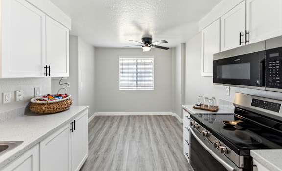 an empty kitchen with white cabinets and black appliances and a ceiling fan