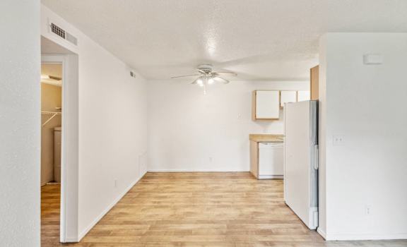 an empty living room with a refrigerator and a ceiling fan