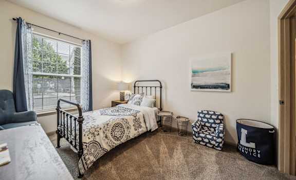 A bedroom with a bed, chair, and window.