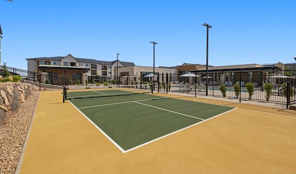 A tennis court is surrounded by a fence and a building.