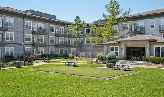 A large grassy area in front of apartment buildings with a tree and benches.