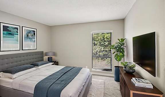 A bedroom with a bed, nightstand, and a window with blinds.