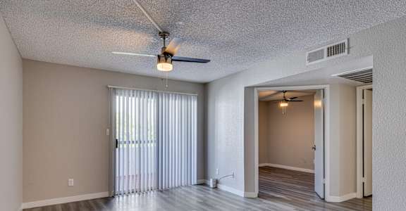 the spacious living room and dining room with sliding glass doors and a ceiling fan at Tides on Southern, Mesa, 85204