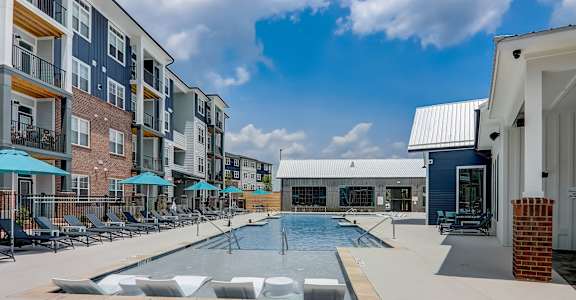 a swimming pool with lounge chairs and umbrellas in front of an apartment building