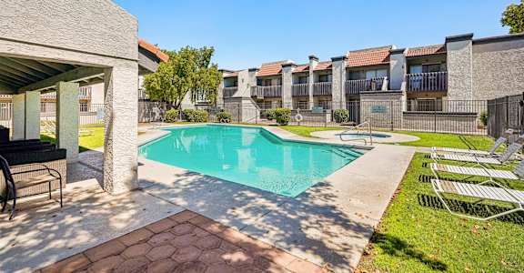 A swimming pool surrounded by a concrete patio and a grassy area with chairs.