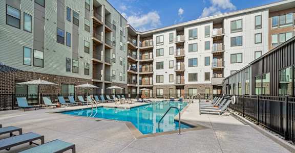 A swimming pool surrounded by apartment buildings and lounge chairs.