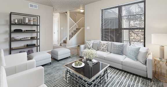 A living room with a white couch, a coffee table, and a staircase in the background.