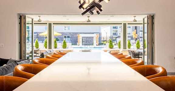 A long white table is surrounded by brown leather chairs in a room with a large window.