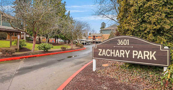 A sign for Zachary Park is in front of a road.