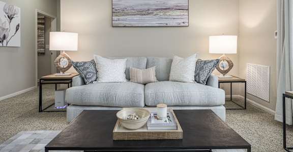 A living room with a grey couch, a coffee table, and a painting on the wall.