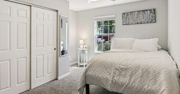 A bedroom with a bed, a ceiling fan, and a window with a view of the city.