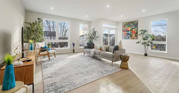 A spacious living room with a grey rug and a large painting on the wall.