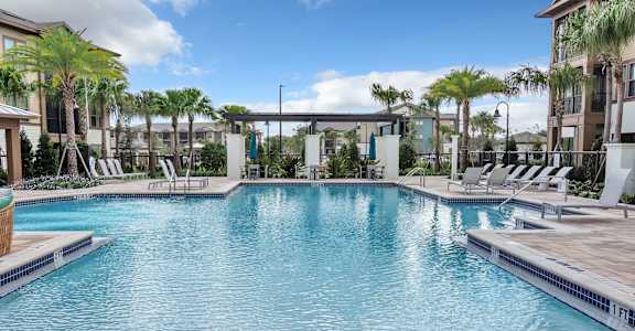 Front view of outdoor pool surrounded by apartment buildings with tropical palms and lounge chairs