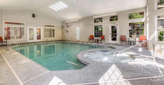 A large indoor swimming pool with a hot tub and lounge chairs.
