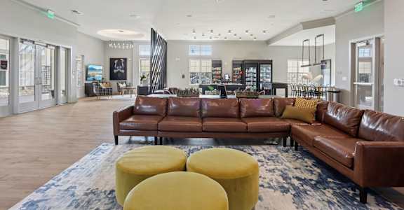 A large brown leather couch is in the middle of a spacious room with a chandelier hanging from the ceiling.