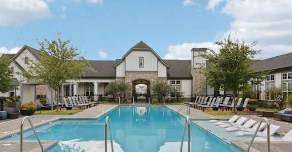 A large swimming pool in front of a house with lounge chairs around it.