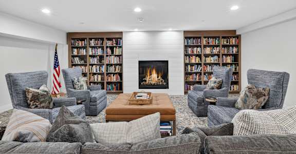 A living room with grey couches, a coffee table, and a fireplace with bookshelves above it.