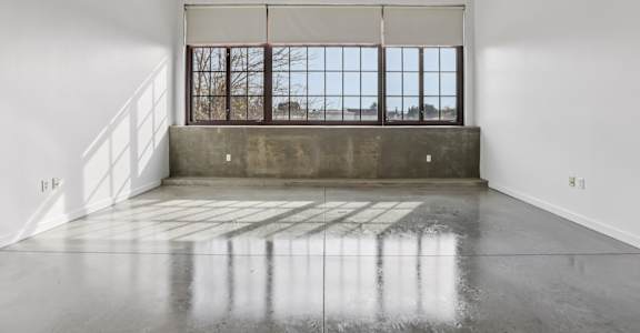A large empty room with a concrete floor and a window with bars.