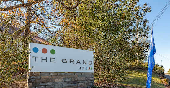 A sign that says "The Grand at 150" is in front of a tree.