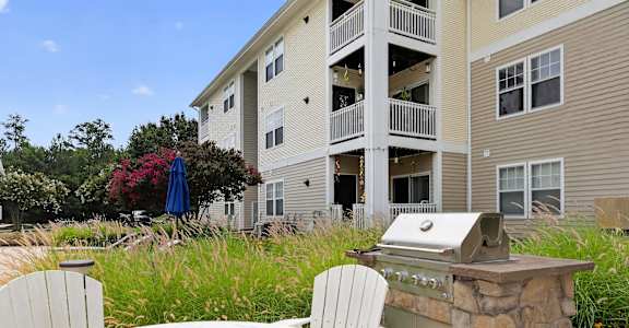 A patio with a grill and chairs in front of a building.
