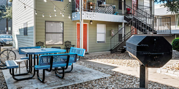 a patio with a table and chairs and a grill in front of a house