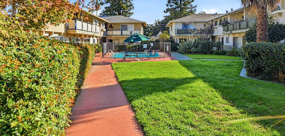 A pathway leads through a grassy area with a tennis court and apartment buildings in the background.