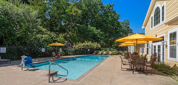 A pool area with a bench and chairs under umbrellas.