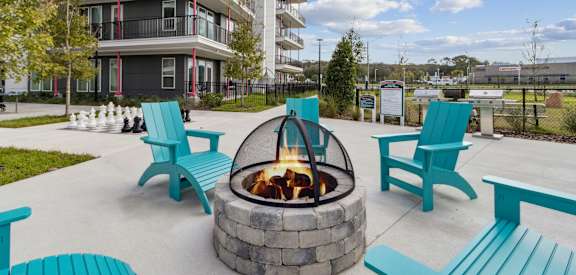 a fire pit with blue chairs in front of an apartment building