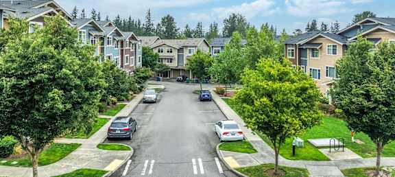 A street view of a residential area with houses on both sides and cars parked along the curb.
