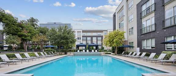 A large swimming pool in a residential area with lounge chairs around it.