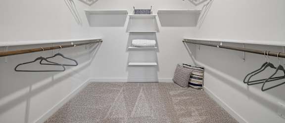 A walk-in closet with white shelves and a grey carpet.