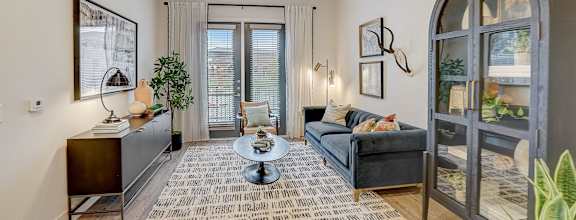 A living room with a black couch, a coffee table, and a large window.