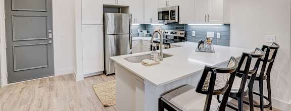 A kitchen with white cabinets and a white island with three chairs.