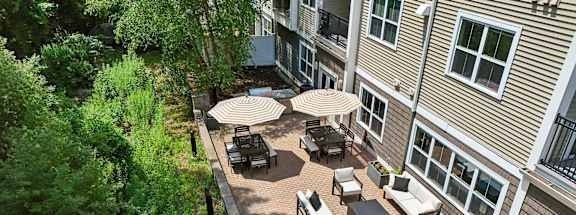 A patio with tables and chairs is surrounded by trees.