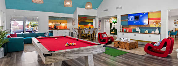 A pool table is in the middle of a room with a TV and a bar at the clubhouse at Fusion Orlando apartments.