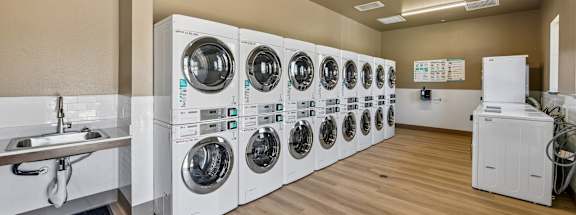 A laundry room with a row of washing machines and a sink.