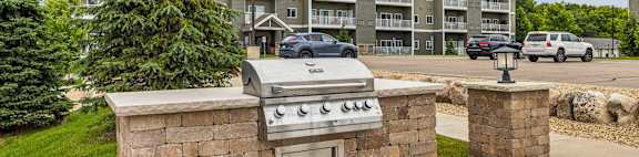 A stone BBQ grill is in the middle of a concrete patio.