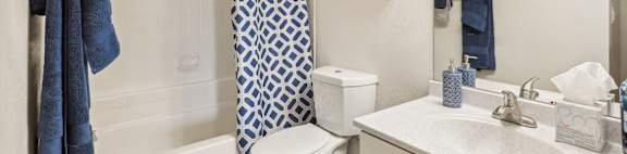 A white bathroom with a blue towel hanging on the shower rod.
