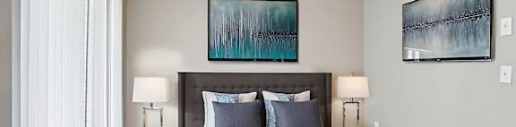 A bedroom with a bed, two lamps, and two paintings on the wall.