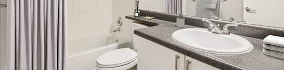 A bathroom with a white toilet, a sink, and a shower with a grey curtain.