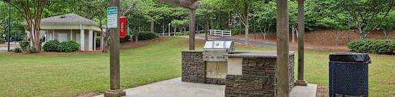 A wooden pergola is over a stone and concrete fireplace.