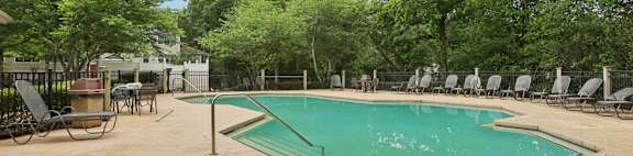 A pool surrounded by trees and chairs.