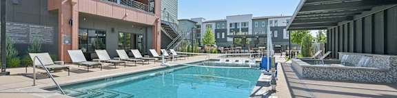 A swimming pool is surrounded by sun loungers and a building.