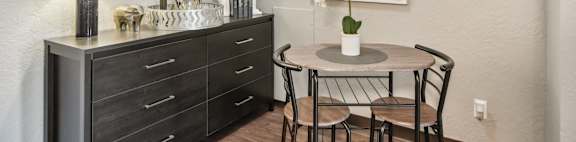 A dining table with chairs and a cabinet with drawers is in a room.