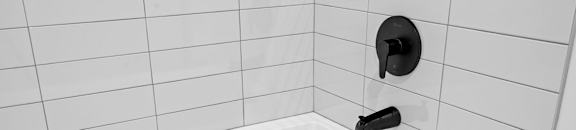 a white tub with a black faucet in a white tiled bathroom