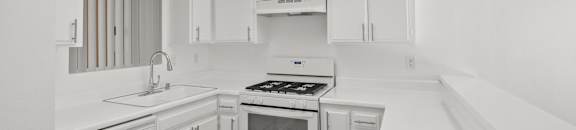A white kitchen with a stove, sink, and cabinets.