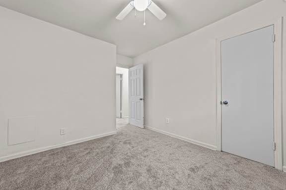 A room with a carpeted floor and a ceiling fan.